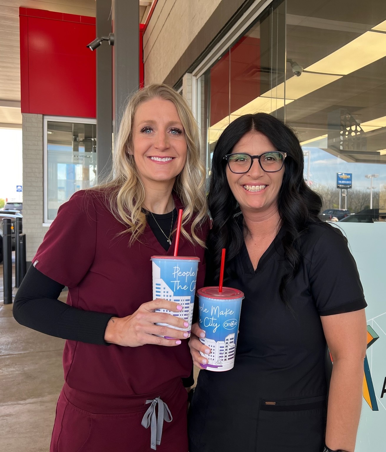 Stillwater Medical labor and delivery nurses Angie and Leslie smiling and holding OnCue charity cups outside of OnCue #8.
