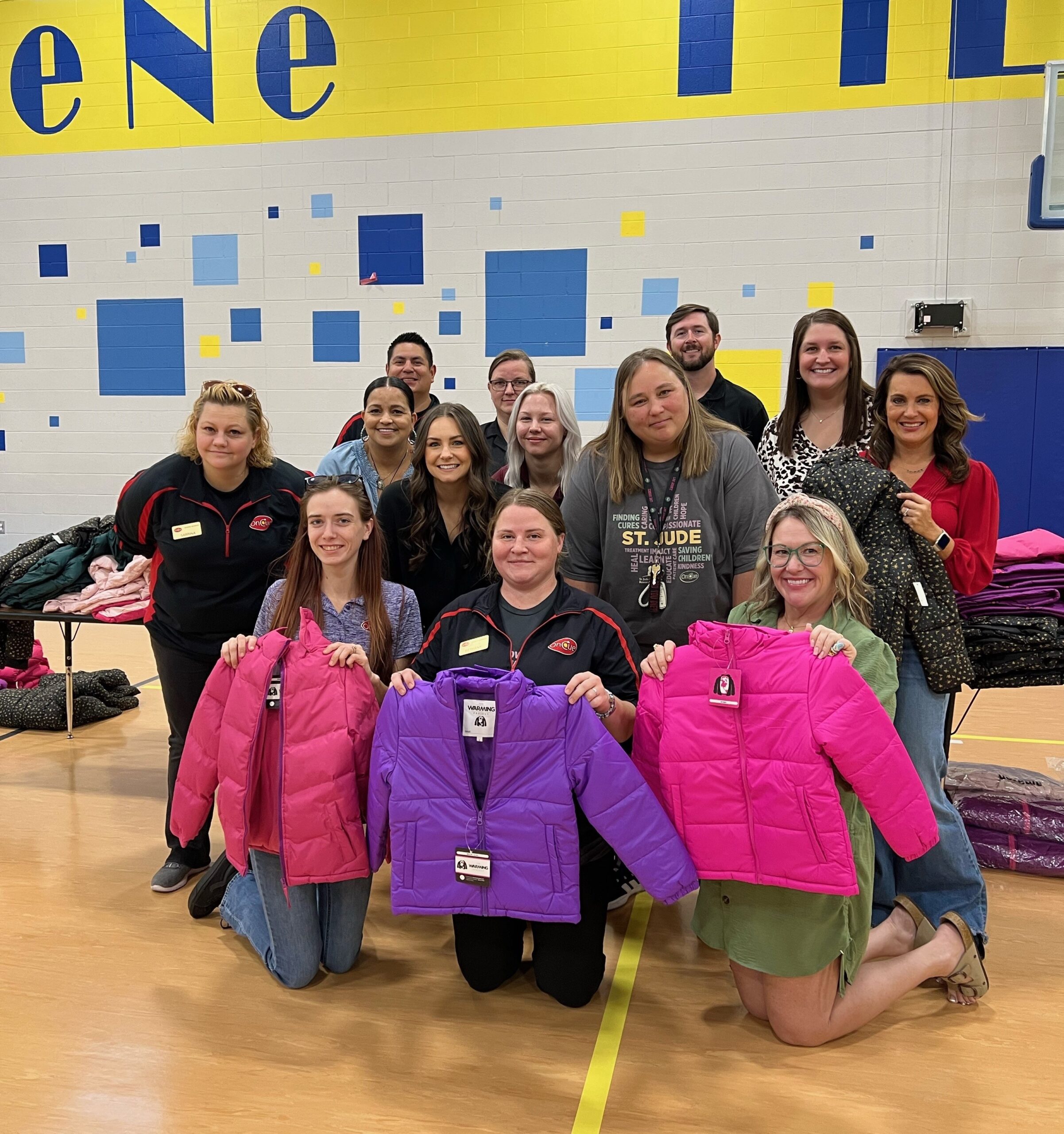 At OKCPS Coat-A-Kid thirteen team members pose with coats for students at Eugene Field Elementary.